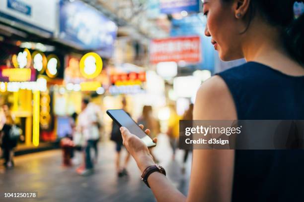 beautiful young woman using smartphone in busy city street, against colourful neon commercial sign and city buildings - consumer journey stock pictures, royalty-free photos & images