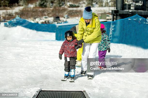 mother helping her young child to get on the magic carpet with his skis, during the winter at a colorado ski resort. - 空飛ぶ絨毯 ストックフォトと画像