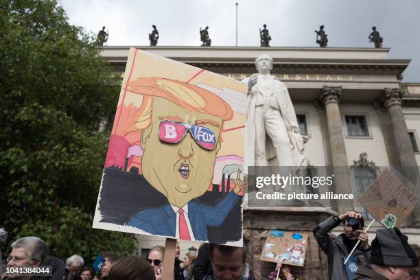 Protestors hold up signs with the picture of US President Donald Trump, who looks through his FOX news and Breitbart news glasses during the "March...
