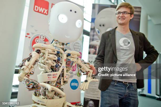 Rafael Hostettler, researcher and head of the 'Roboy' project, poses next to a humanoid robot named 'Roboy' during the 'DWX - Developer Week'...