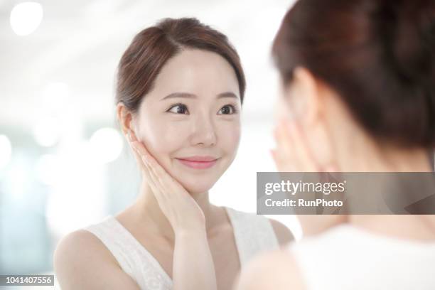 young woman touching face in front of mirror - beauty routine stock pictures, royalty-free photos & images