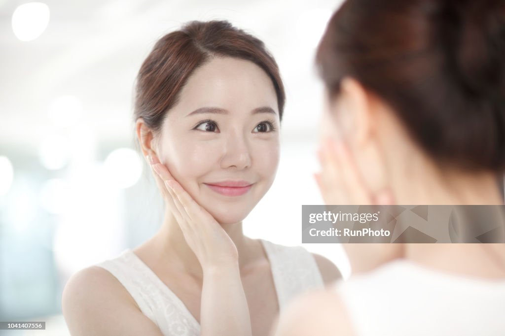 Young woman touching face in front of mirror