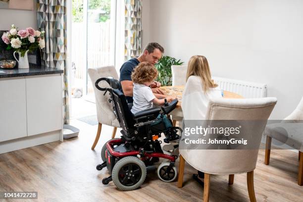 garçon en fauteuil roulant fait scie à découper avec les parents - chaise roulante photos et images de collection