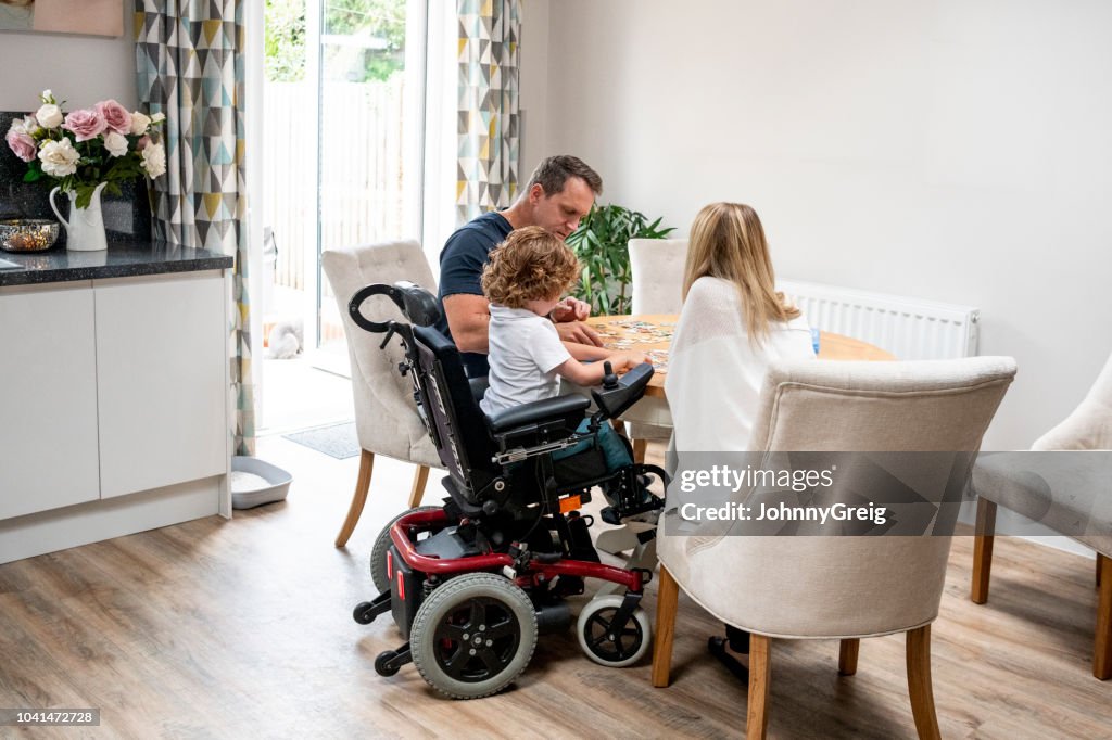 Boy in wheelchair doing jigsaw with parents