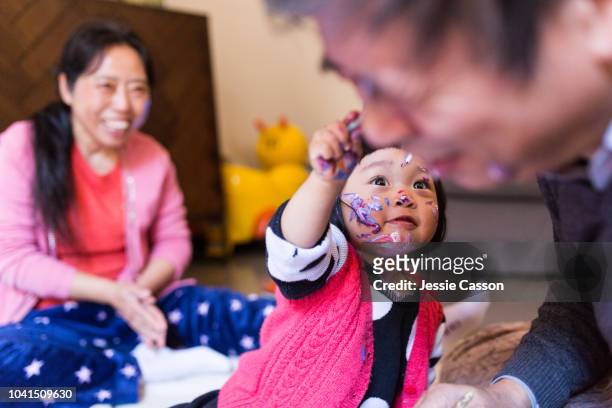 Grandparents and child having fun with paint on her face