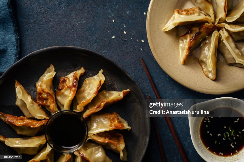 Fried gyoza dumplings with duck served with soy sauce ans sesame seeds. Dark blue concrete background