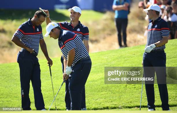 Golfer Tiger Woods smiles with a tuft of grass on his head placed there by US golfer Justin Thomas as US golfer Patrick Reed plays a shot while US...