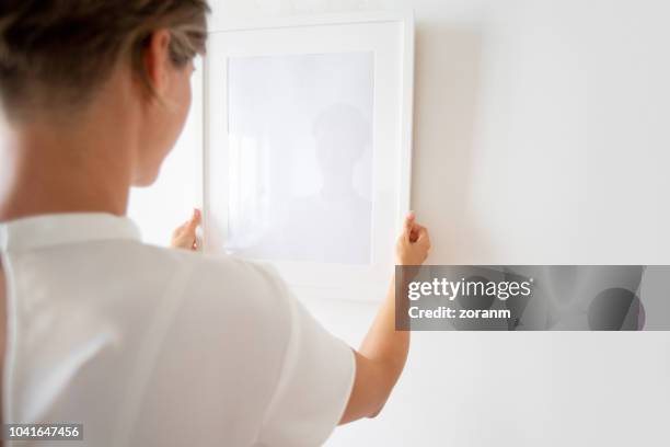 woman hanging picture frame - hanging picture frame stock pictures, royalty-free photos & images