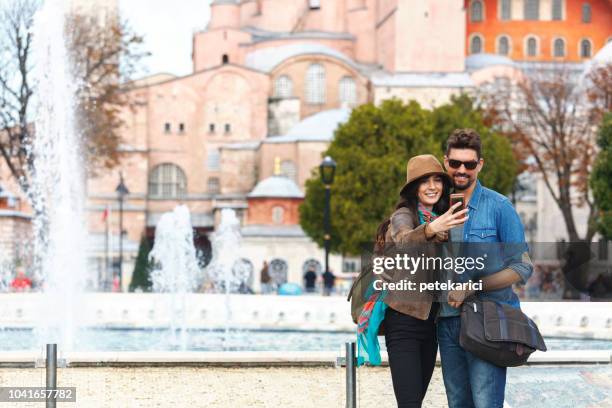 cheerful young couple taking a selfie, in front of the hagia sofia mosque in istanbul - tourist istanbul stock pictures, royalty-free photos & images