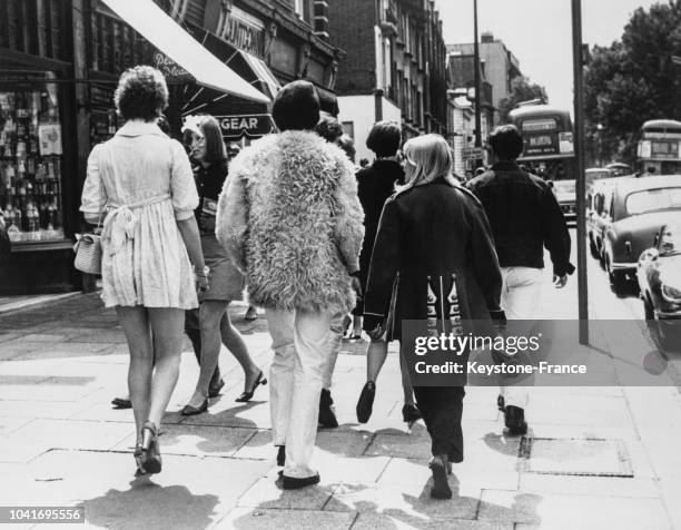 Couple marchant à Chelsea, la femme est en pantalon et veste militaire, l'homme porte un épais blouson en fourrure malgré la chaleur, à Londres,...