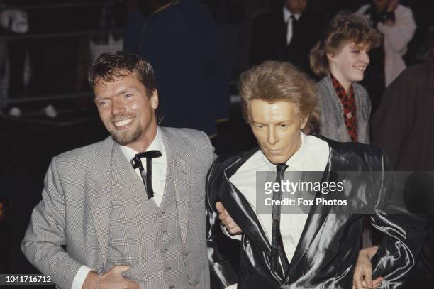British entrepreneur Richard Branson with a waxwork of singer David Bowie at the premiere of the film 'Absolute Beginners', London, April 1986.