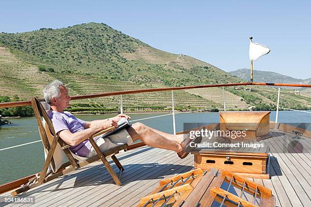 senior man reading book on a boat holiday - schiffsdeck stock-fotos und bilder