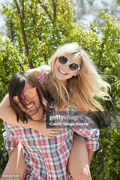 young man giving young woman piggyback - hollywood couples stock pictures, royalty-free photos & images