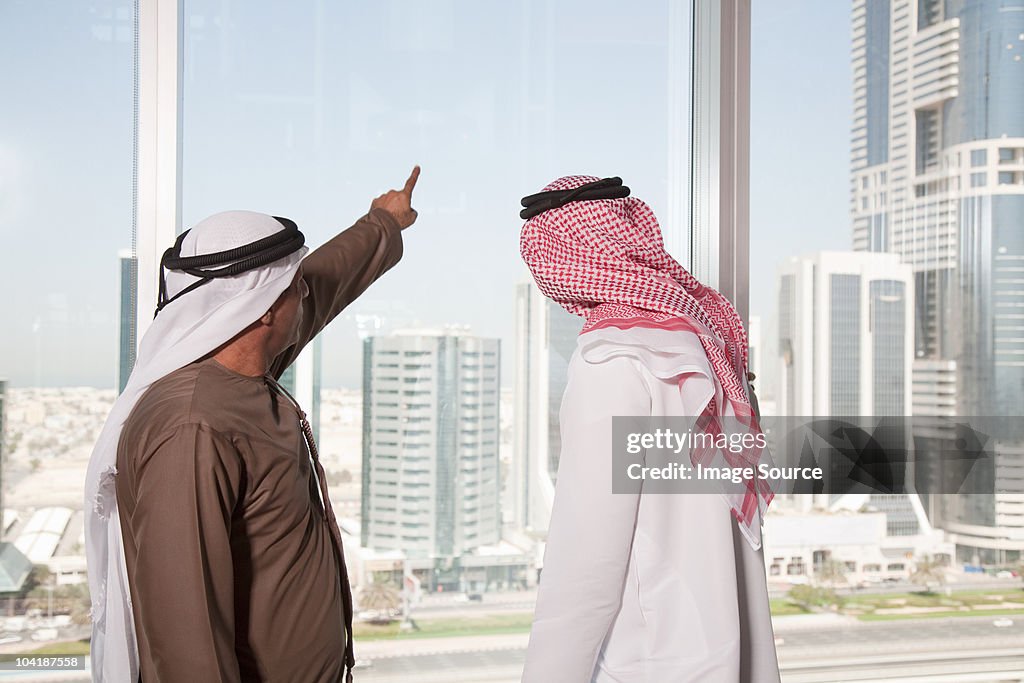 Middle eastern businessmen looking at dubai through office window