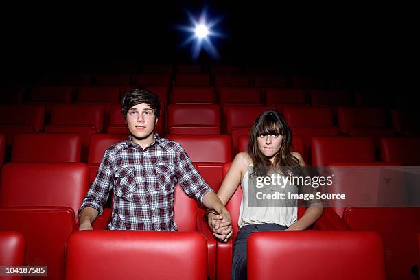 junges paar holding hände in movie theater - kinositz stock-fotos und bilder