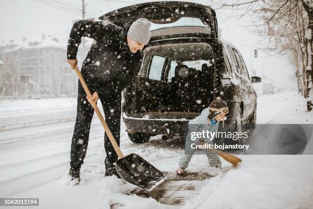 father and little son cleaning snow around car - shovel stock pictures, royalty-free photos & images