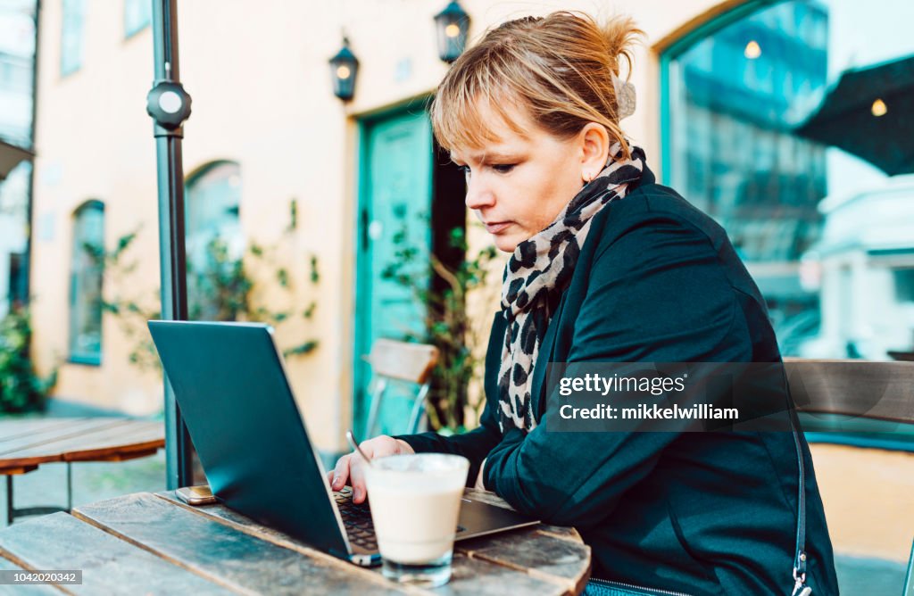 Woman sits at outdoor cafe using her laptop computer