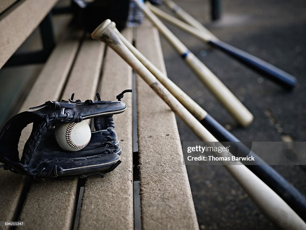 Baseball glove with ball and bats in dugout