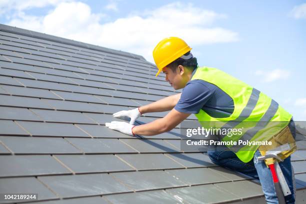 builder working on roof of new building, construction worker wearing safety harness and safety line working on roof new warehouse. - costruttore di tetti foto e immagini stock