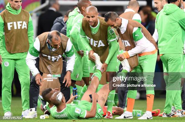 Sofiane Feghouli of Algeria lies on the ground and gets a massage by team-mates to prevent a cramp during the FIFA World Cup 2014 round of 16 soccer...