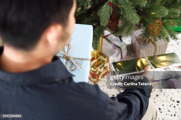 man placing presents under a christmas tree - christmas presents under tree stock pictures, royalty-free photos & images