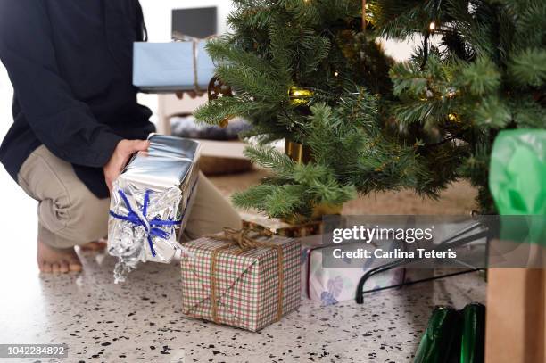 man placing presents under a christmas tree - christmas presents under tree stock pictures, royalty-free photos & images