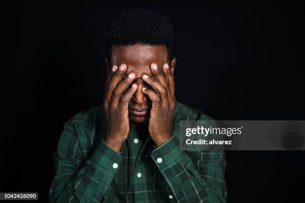 betonte afrikanischen mann auf schwarzem hintergrund - kopf in den händen stock-fotos und bilder