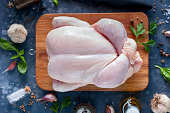 Prepared fresh raw chicken for cooking on a cutting wooden board, top view, selective focus