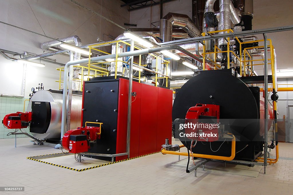 A brightly lit boiler room with red and black gas boilers