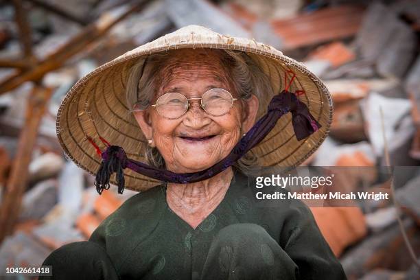 a elderly local woman smiles as she takes a break from work in bai xep; a quiet remote fishing village off the tourist path, 10km from the major city of qui nhon. - vietnamese stock-fotos und bilder