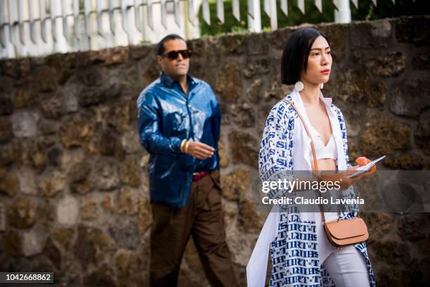 Guest, wearing a white bralette, white trousers, printed jacket, Loewe crossbody bag and orange gloves, is seen before the Loewe show on September...