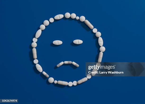 pills forming frowning face on blue background - prescription drugs dangers stock pictures, royalty-free photos & images