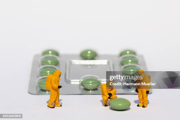 small scientists in clean suits examining green pill from blister pack - prescription drugs dangers stock pictures, royalty-free photos & images