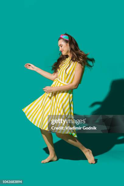 portrait carefree young woman in striped dress dancing against turquoise background - jurk stockfoto's en -beelden