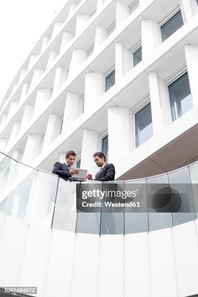 poland, warzawa, two businessmen with tablet computer standing in front of hotel - balustrade stock photos et images de collection