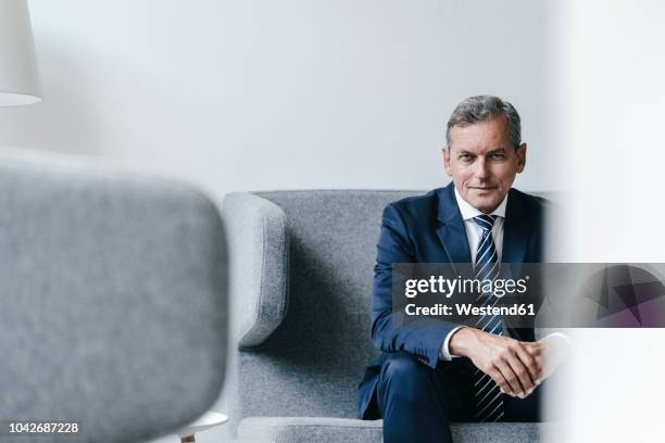 portrait of mature businessman sitting on couch in his office - office sofa stock-fotos und bilder