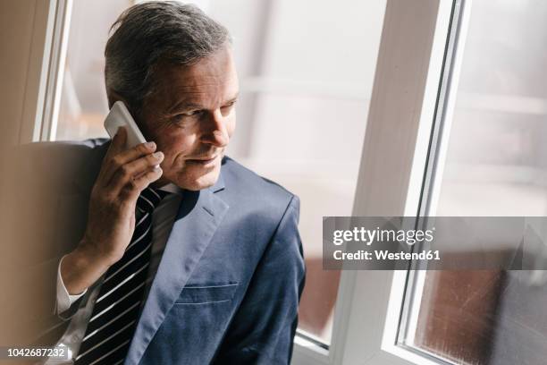 smiling mature businessman on cell phone looking out of window - contact list stock-fotos und bilder
