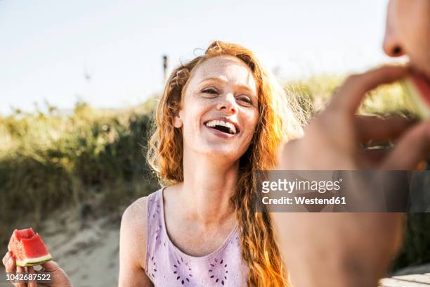 netherlands, zandvoort, happy woman eating watermelon looking at man on the beach - 30s woman eating stock pictures, royalty-free photos & images