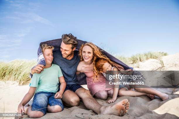 netherlands, zandvoort, happy family under a blanket on the beach - protect family stockfoto's en -beelden