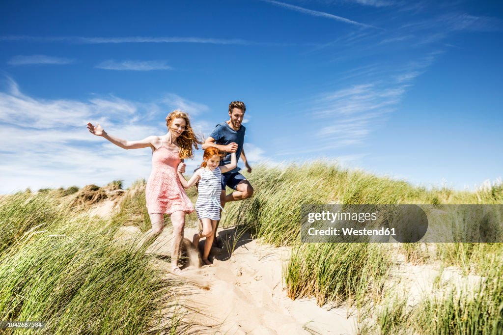 Netherlands, Zandvoort, happy family with daughter running in beach dunes