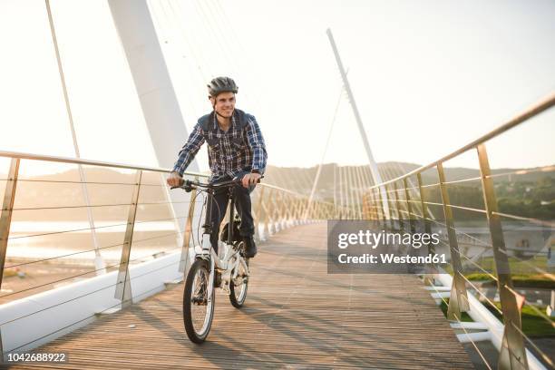 young man riding bicycle on a bridge at sunset - athleticism stockfoto's en -beelden