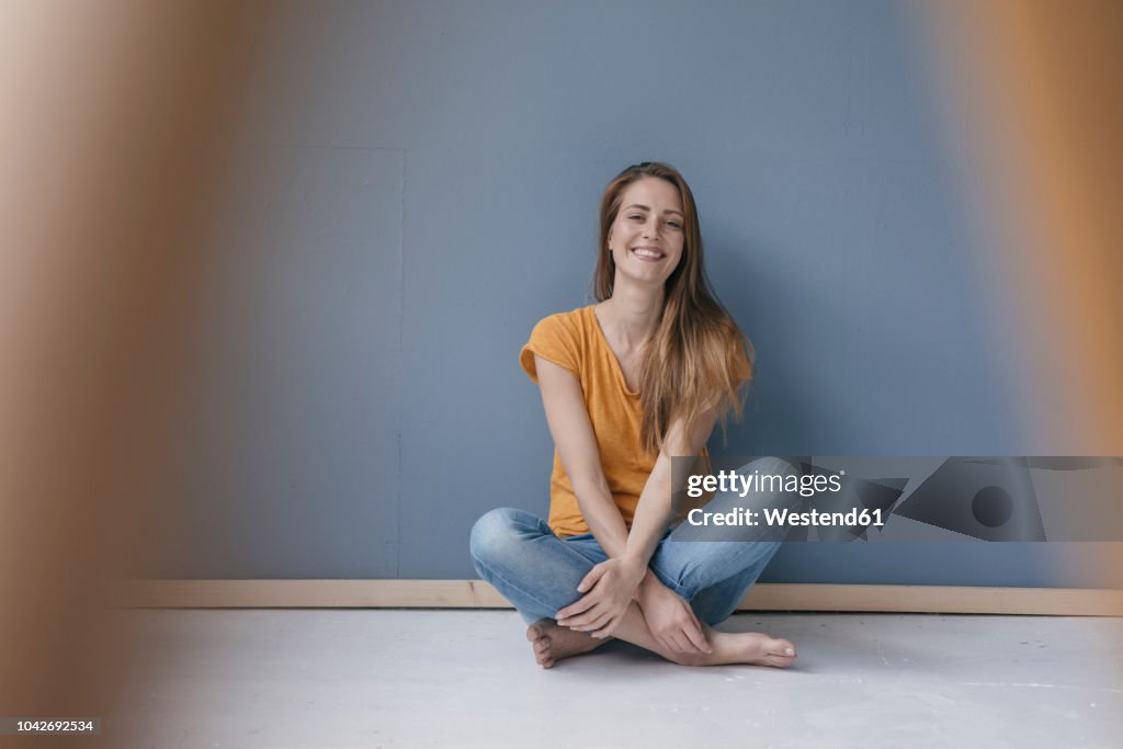 Happy woman sitting on ground, barefoot with legs crossed, laughing