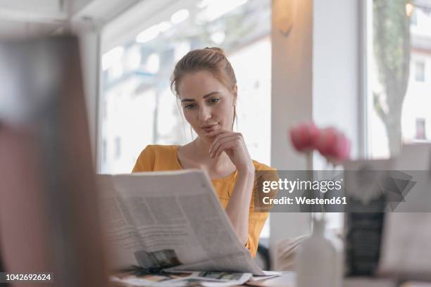 young woman sitting in coworking space, reading newspaper - mujeres de mediana edad fotografías e imágenes de stock
