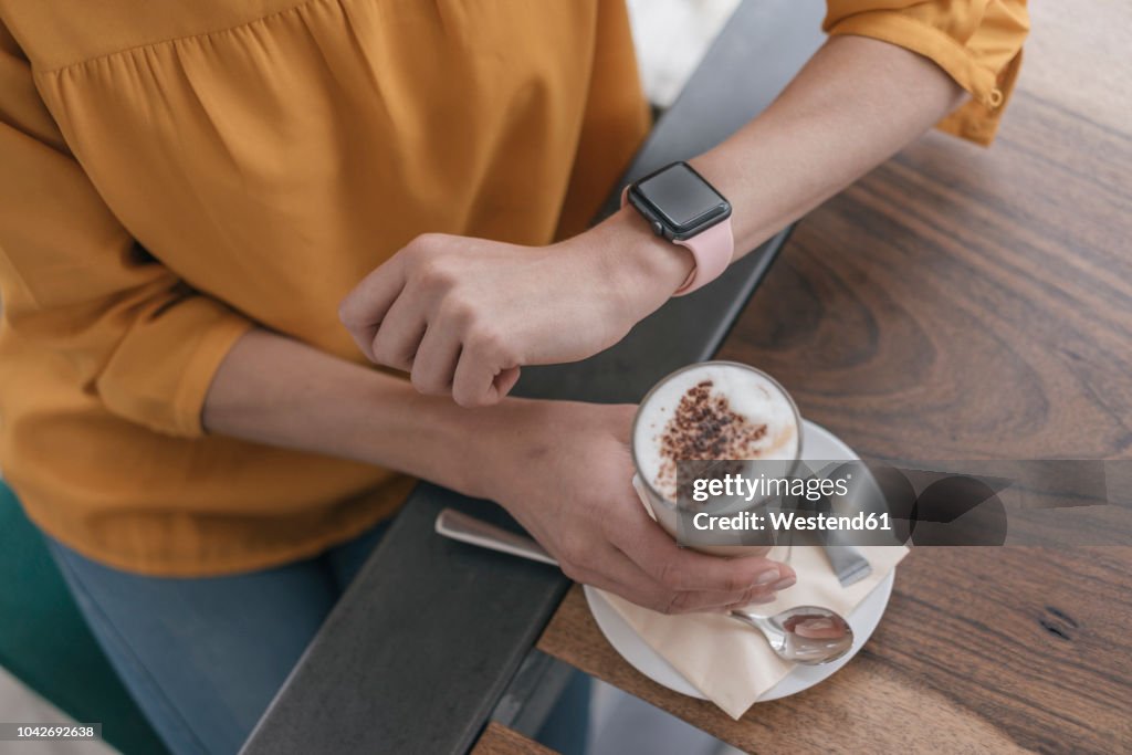 Woman wearing smartwatch, sitting in cafe, drinking coffee