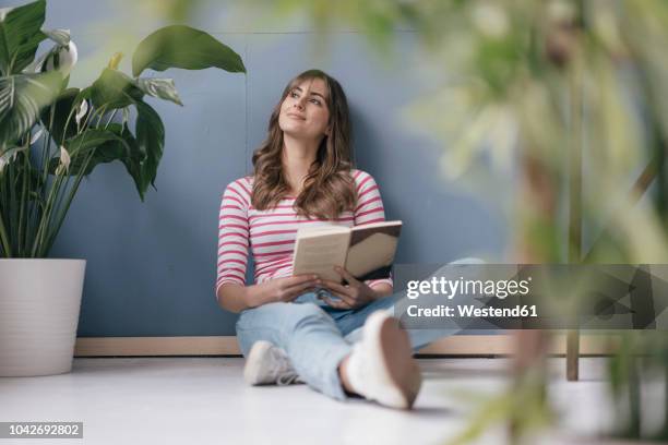 woman sitting on ground in her new home, reading a book, surrounded by plants - art books stock-fotos und bilder