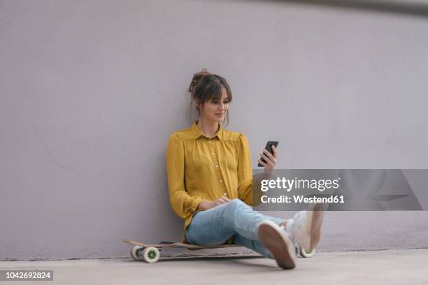 young woman sitting on skateboard, using smartphone - sitting and using smartphone studio stock pictures, royalty-free photos & images