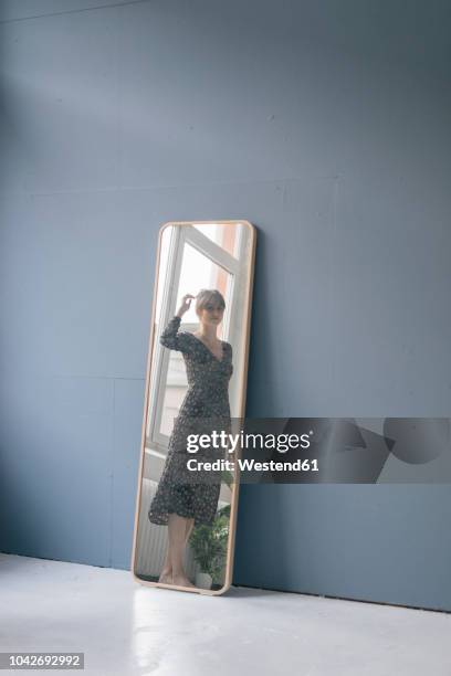 young woman in vintage dress looking into mirror - full length mirror stock-fotos und bilder