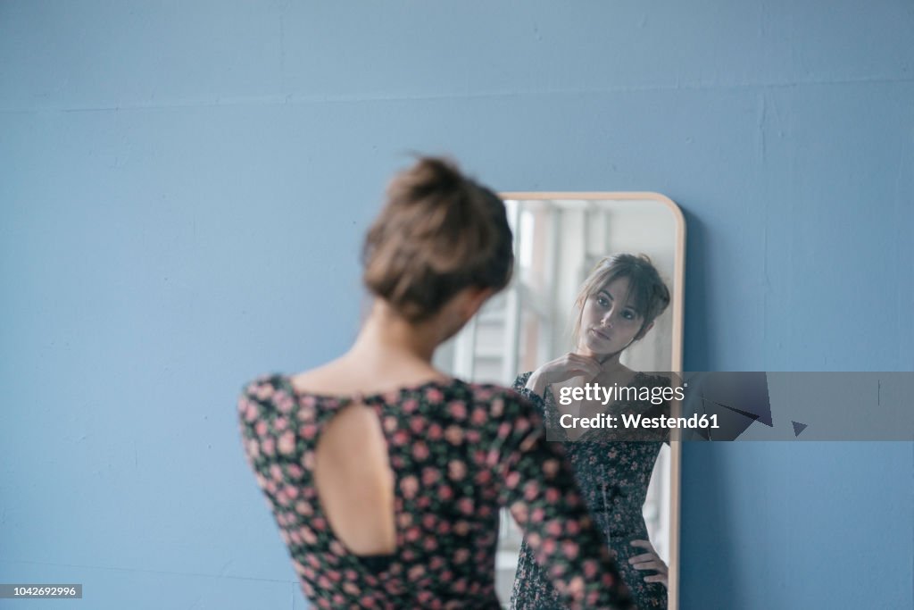 Young woman in vintage dress looking into mirror