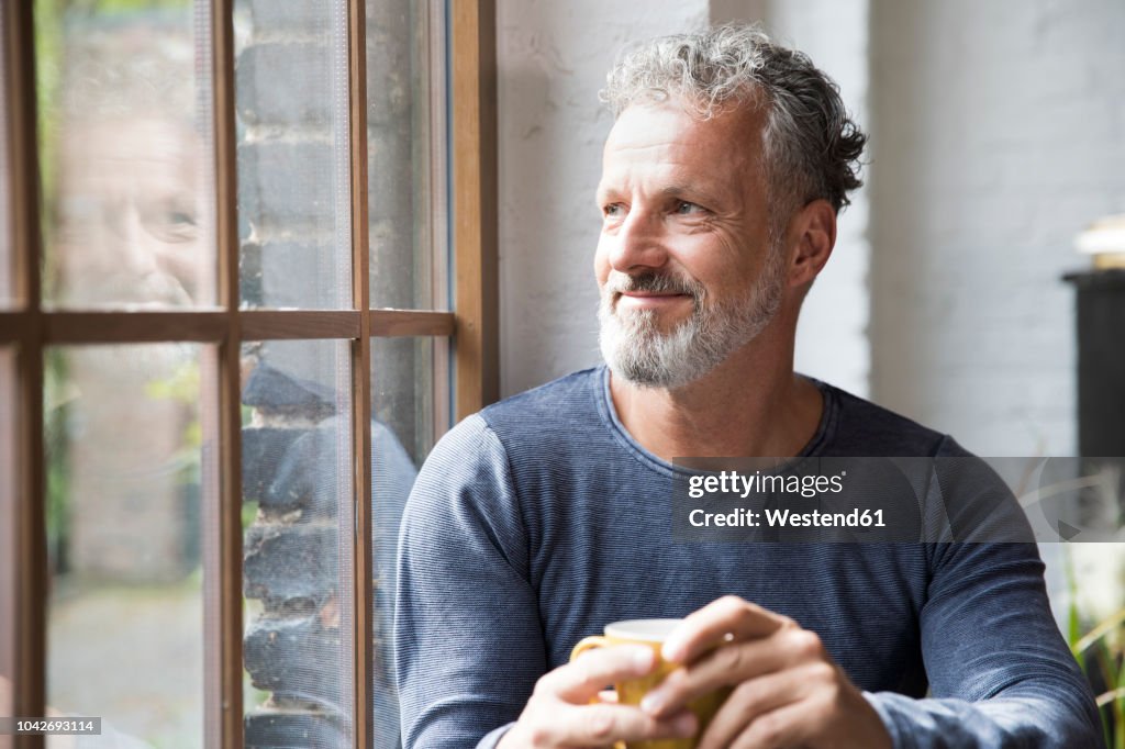 Mture man taking a break, drinking coffee at the window of his loft apartment