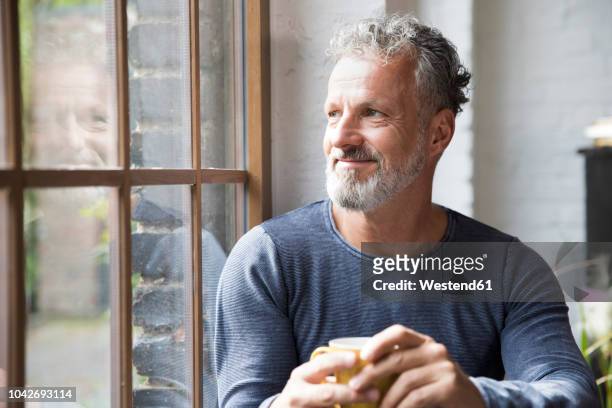 mture man taking a break, drinking coffee at the window of his loft apartment - männer über 40 stock-fotos und bilder
